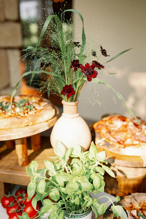 Wedding catering display with pizza wedding catering on wooden boards, tomatoes and basil, red flowers in a ceramic vase on a sunlit patio