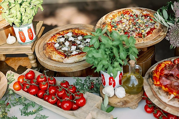 Pizza wedding buffet spread on wooden boards with fresh tomatoes and basil accent on an outdoor table, styled with garlic and olive oil
