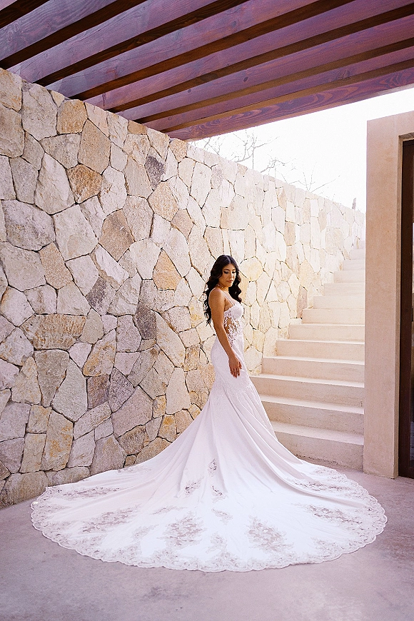 Bridal portrait of a bride in a lace train wedding dress, side profile on stairs by a stone wall with wooden ceiling beams overhead