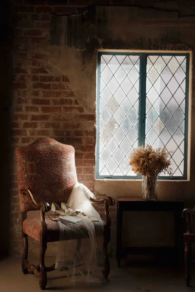 Bridal accessories with wedding shoes flat lay on a vintage chair, veil and jewelry beside a bouquet in a vase by a brick wall window