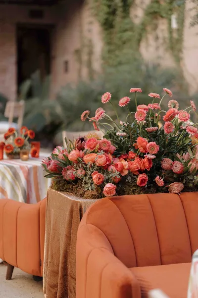 Reception lounge decor with wedding lounge seating, featuring an orange velvet sofa, lush florals, and taper candles in a courtyard setting