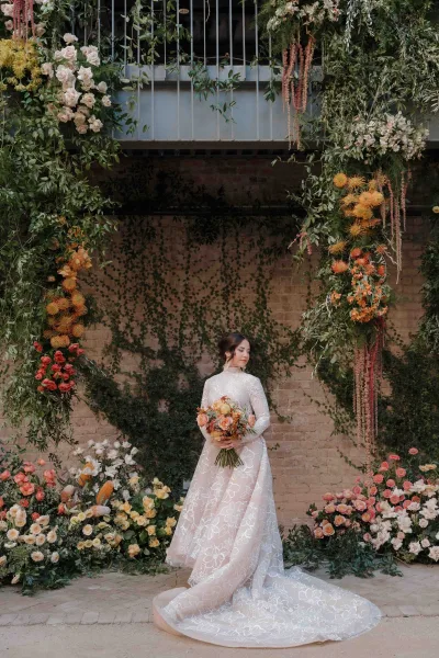 Bridal portrait of bride holding bouquet in a long sleeve lace wedding dress with cathedral train before an ivy brick courtyard arch