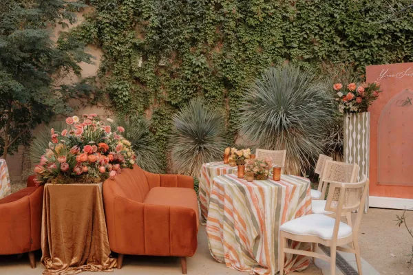 Wedding lounge decor with wedding lounge seating, featuring a rust velvet sofa, striped tablecloth, florals and candles by an ivy wall