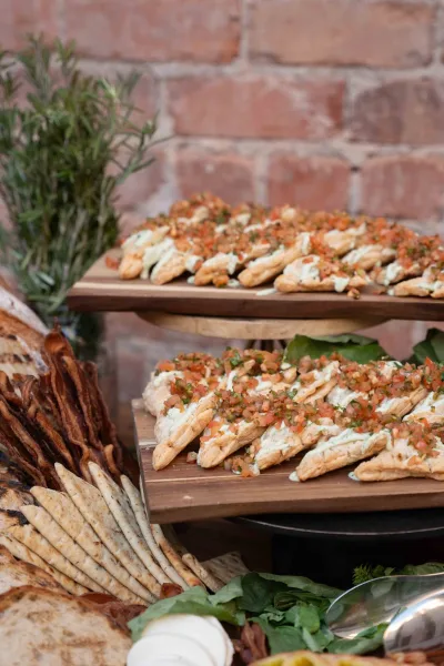 Wedding appetizer display with cocktail hour appetizers on wood serving stands, flatbread and bread with dips and herb garnish against a brick wall