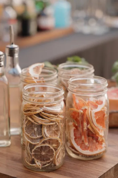Drink garnish jars with dried citrus drink garnish, filled with orange, grapefruit, and lemon slices on a wooden board at a bar counter