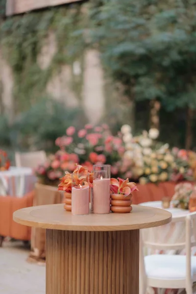 Cocktail table decor with wedding cocktail hour decor featuring floating candles in glass cylinders and peach florals on a wooden table in a garden setting