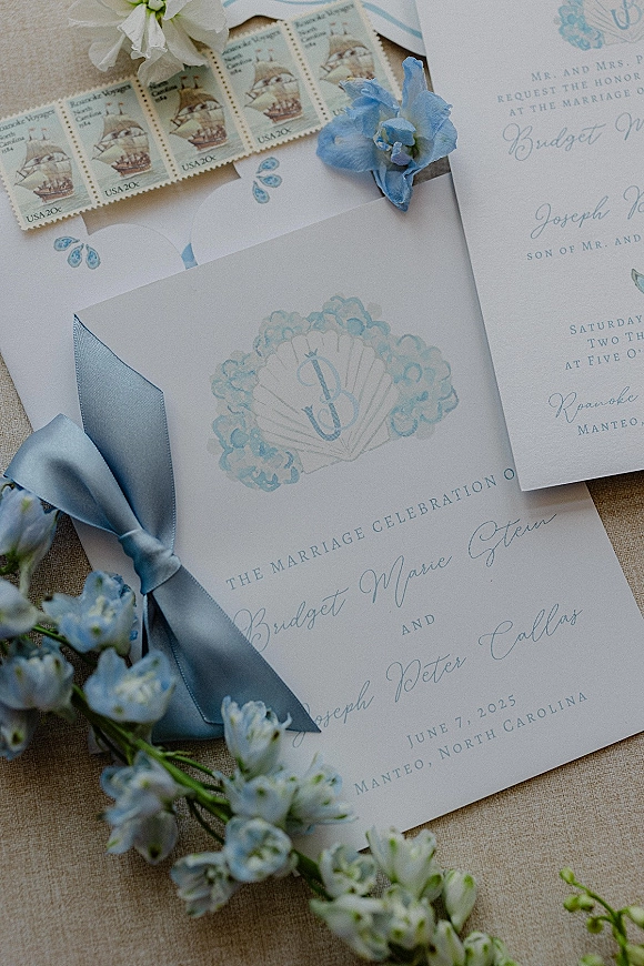 Wedding invitations and wedding invitation suite arranged on linen with blue satin ribbon, wax seal, vintage stamps, and a small floral sprig