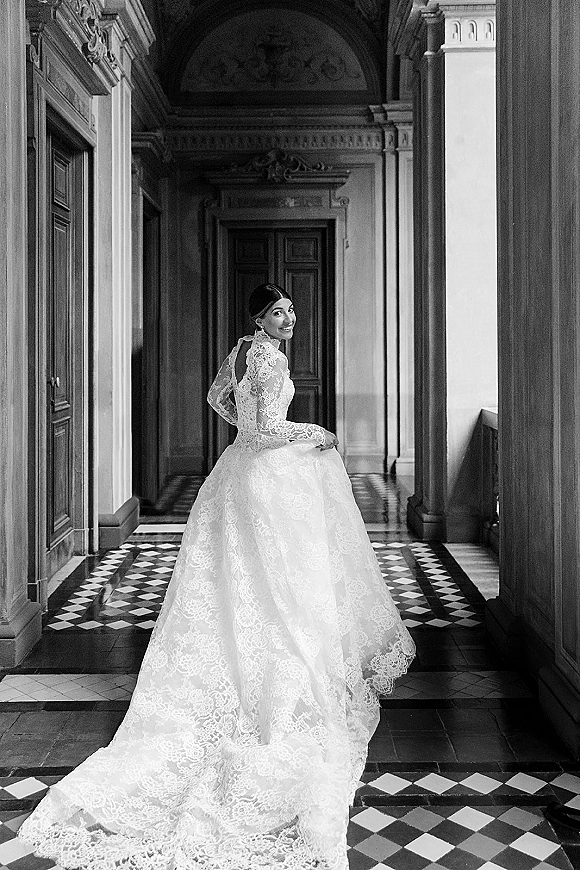 Bridal portrait of a bride looking back in a lace wedding dress with cathedral train and veil in an ornate hallway with checkered floor