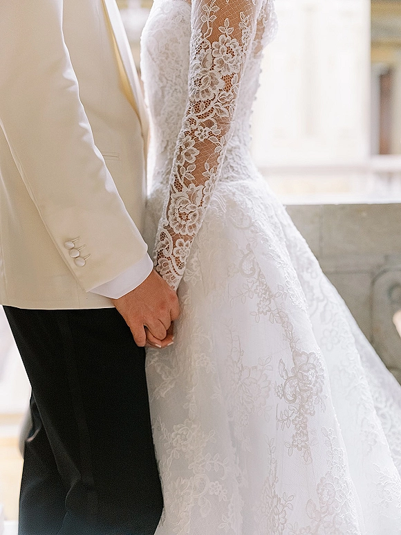 Wedding couple portrait of bride and groom holding hands, showcasing lace sleeve gown and white dinner jacket in soft window light indoors