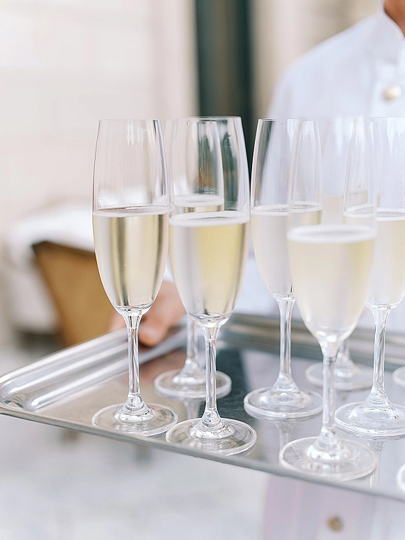 Champagne toast with wedding champagne flutes filled with sparkling wine on a serving tray held by a waiter indoors