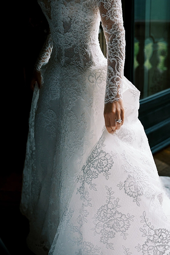 Wedding dress with lace wedding dress details, long sleeves and illusion neckline, shown in soft window light against an interior wall
