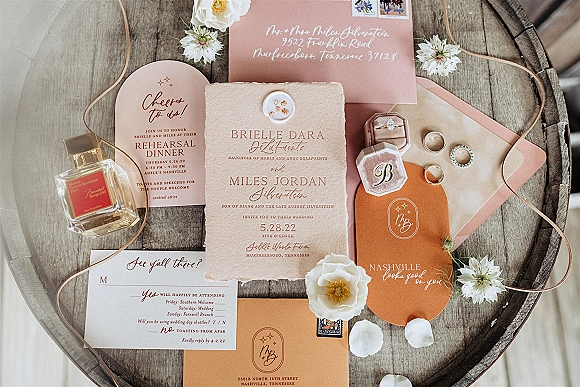 Wedding invitation suite with blush wedding invitations, wax seal, stamps, ring box, jewelry and petals arranged on a wood surface