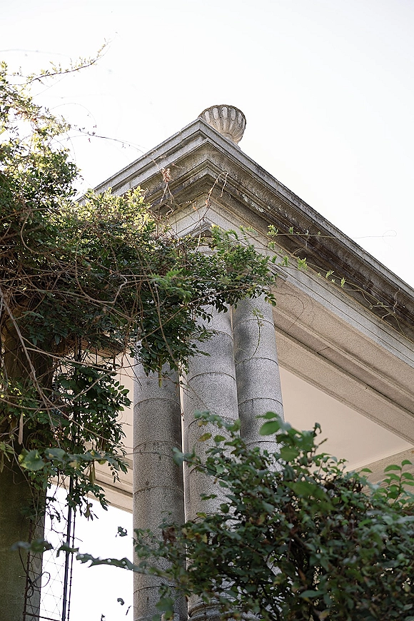Wedding venue exterior with ivy vines climbing stone columns, showcasing a neoclassical facade beneath a bright white sky