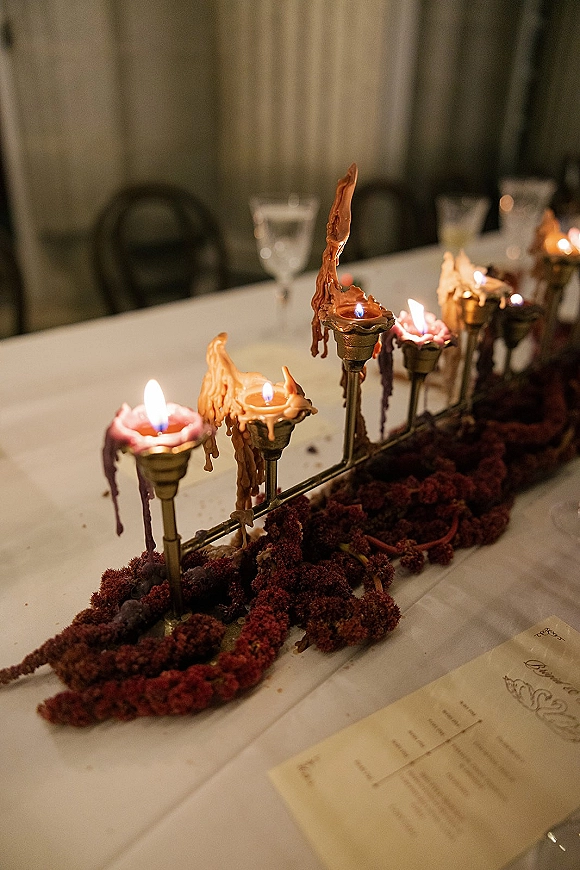 Wedding table centerpiece with candlelit wedding centerpiece glow, brass candelabra and taper candles with wax drips on a garland runner
