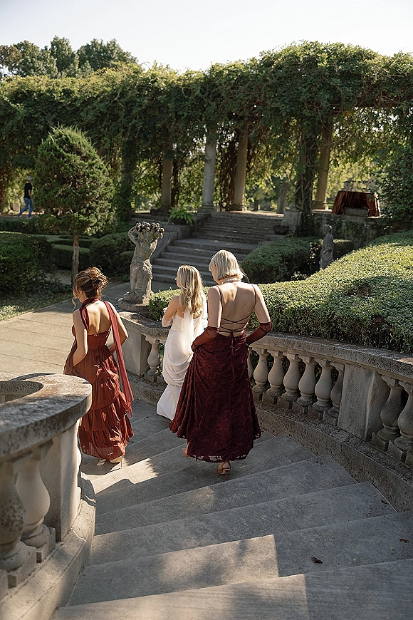 Bridesmaid group walking down stairs with the bride, wearing mismatched dresses and long gloves on a stone staircase in a garden terrace