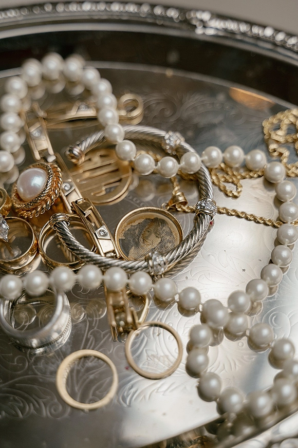 Wedding rings close up, stacked mixed-metal bands with diamond accent on an engraved metal surface beside a pearl necklace and jewelry tray