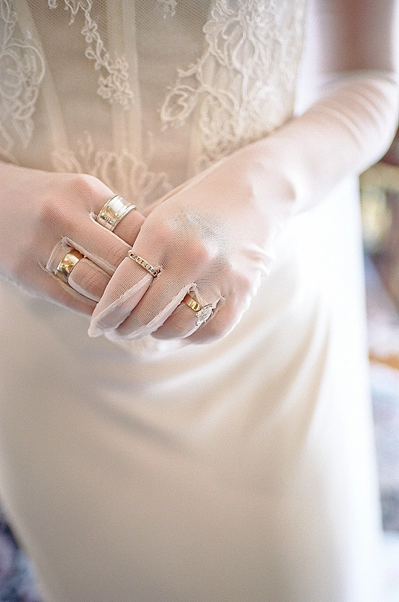 Wedding rings and engagement ring close-up showing a diamond solitaire stacked with a gold band against lace wedding dress in soft indoor light