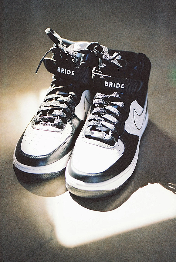 Bride sneakers in black and white with laces and an embroidered label on a concrete floor, lit by window light and shadows