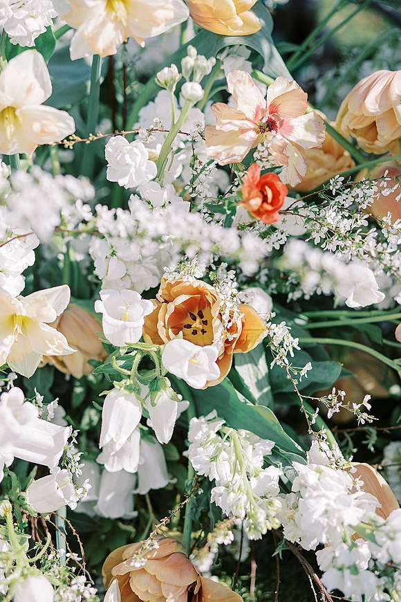 Wedding florals with peach and white wedding flowers, featuring peach tulips and baby's breath nestled in airy greenery against soft greenery backdrop