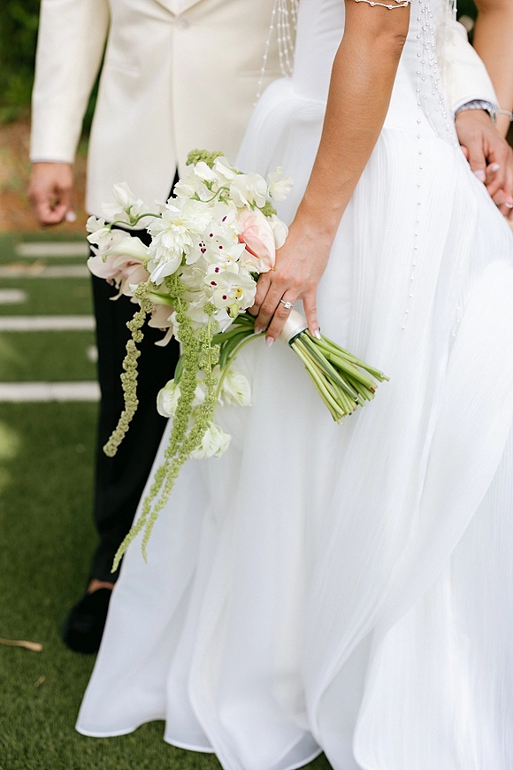 Bridal bouquet with white cascading bouquet of calla lilies and orchids, satin ribbon wrap, held by bride in pearl-strap dress on garden steps