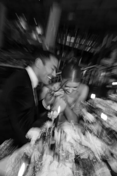 Reception couple moment with bride and groom laughing at a dim candlelit dinner table, wedding ring visible beside floral centerpiece
