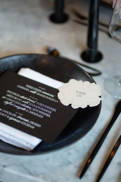 Wedding place setting with black and white place setting details, featuring a menu card, place card, white napkin, and candles on marble tabletop