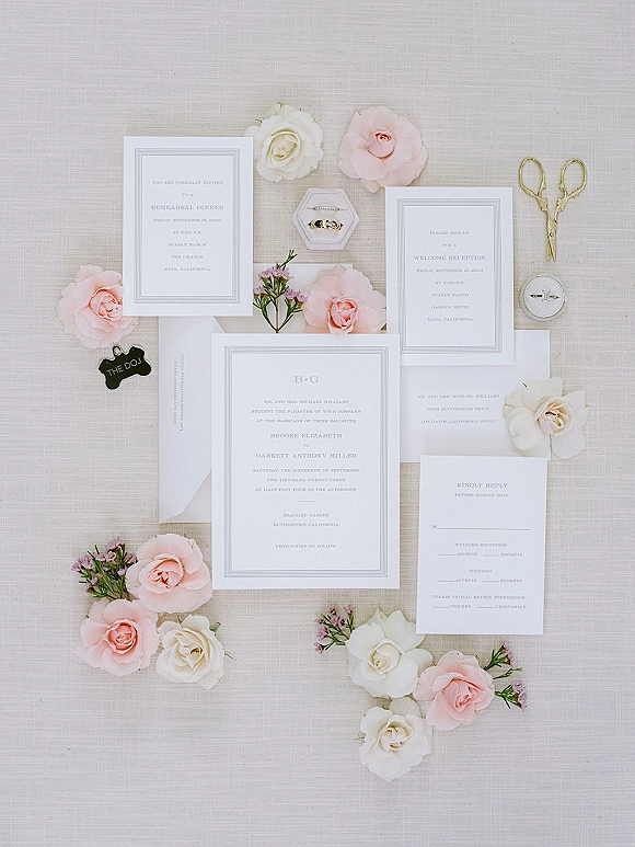 Invitation suite wedding invitation flat lay with cards and envelopes, wax seal, rings in a box, vintage scissors, and blush roses on linen backdrop