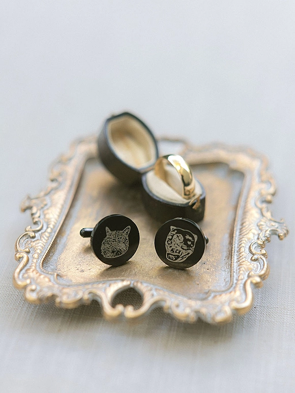 Wedding rings in a black ring box beside engraved cufflinks and a gold wedding band on a vintage silver tray over linen fabric