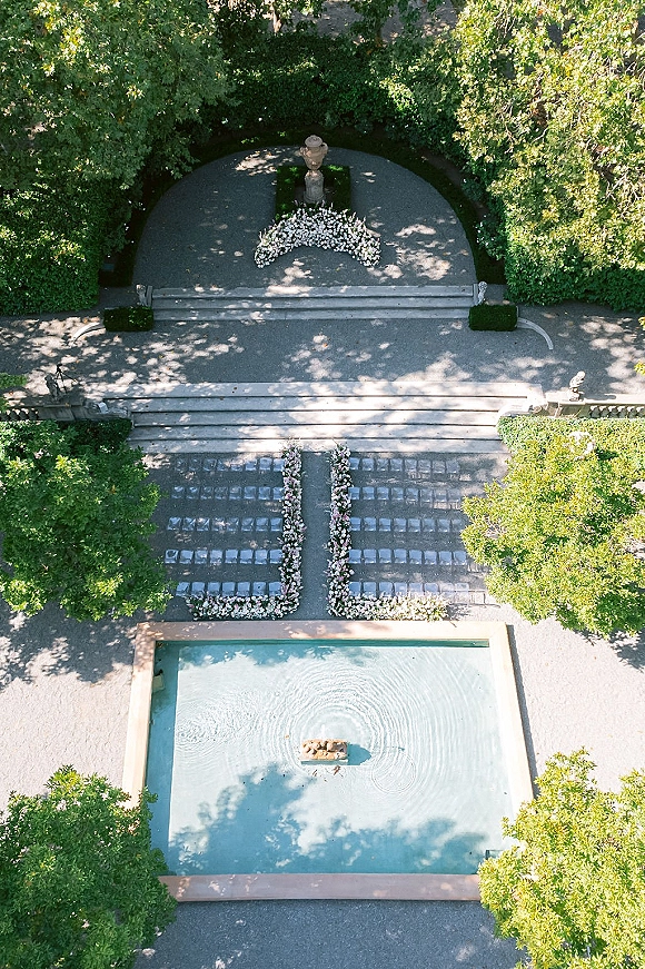 Ceremony aisle decor with floral lined wedding aisle, white floral arrangements framing stone steps beside a fountain and reflecting pool