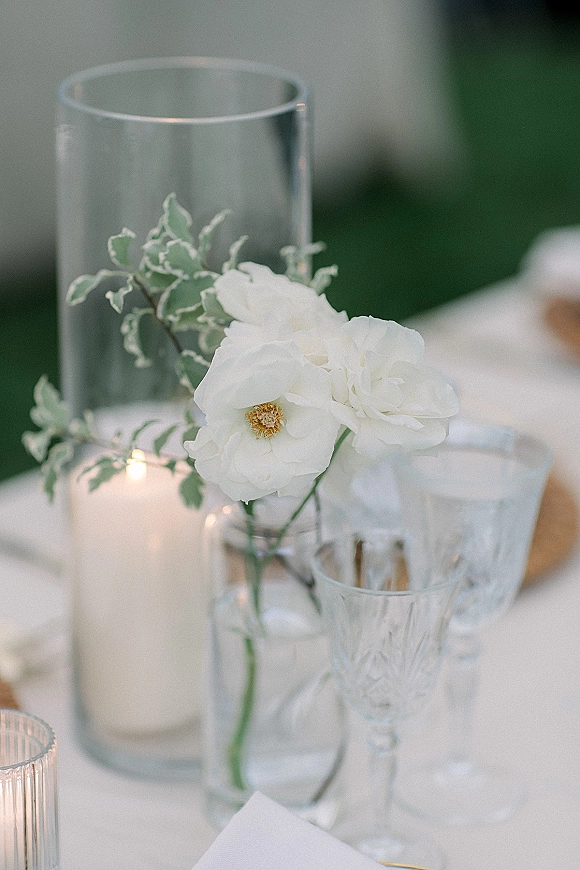Wedding tablescape with a white wedding centerpiece in glass vases and votive candles, crystal goblets on a white tablecloth by a green wall