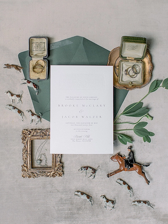 Invitation suite wedding invitation flat lay with green envelopes, rings in vintage boxes, eucalyptus, and brass tray on linen backdrop