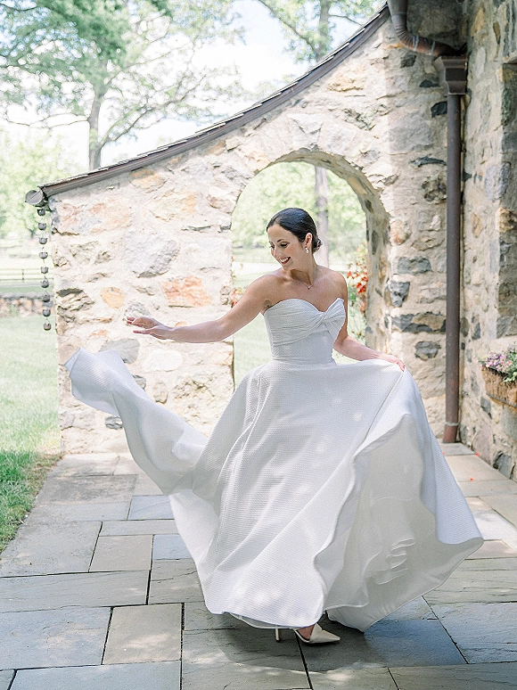 Bridal portrait of a bride twirling her strapless wedding dress, full skirt swirling under a stone archway on a patio path