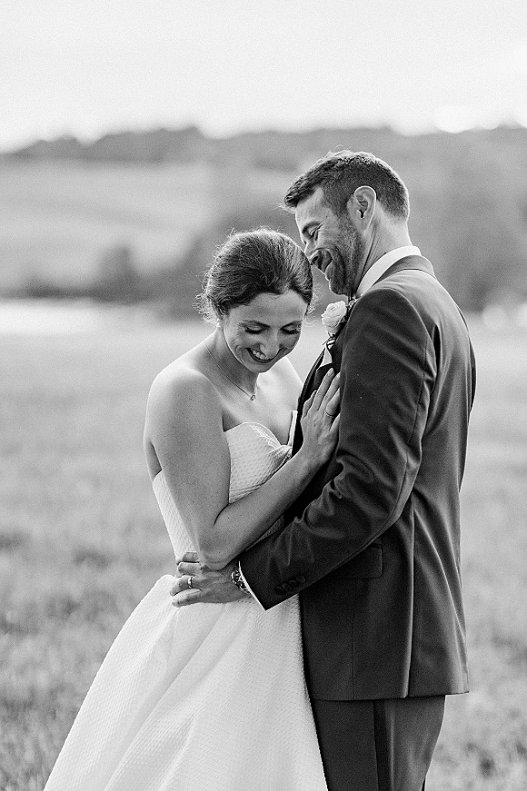 Couple portrait in a black and white wedding portrait style, bride and groom hugging in a field with hills and trees behind them