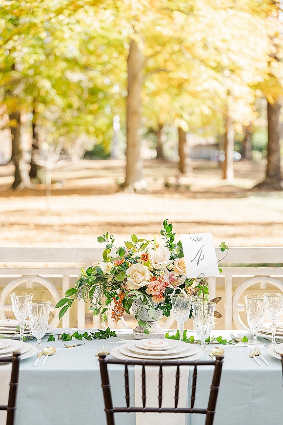 Reception tablescape with outdoor reception table styling, lush floral centerpiece and greenery garland on a white tablecloth in an autumn garden setting