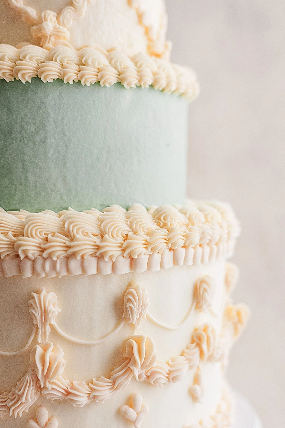 Wedding cake with tiered wedding cake design, buttercream frosting piped rosettes and swags showcased against a neutral backdrop