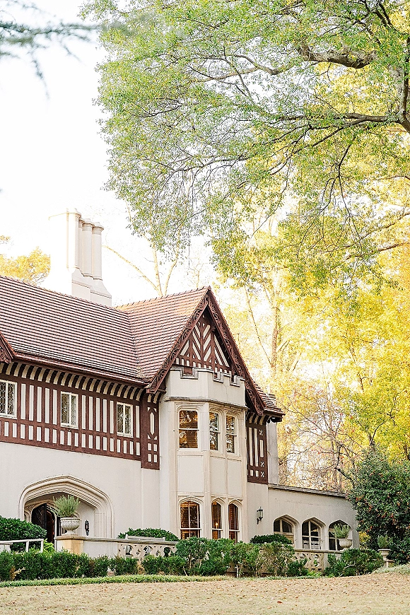 Wedding venue exterior with Tudor-style facade, multi-pane windows and chimneys, flanked by hedges and urns along a gravel drive