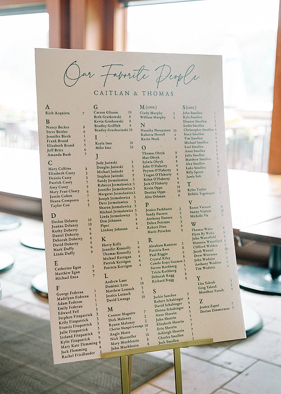 Wedding seating chart sign on an easel with alphabetical seating chart layout, set by bright windows in a naturally lit indoor venue
