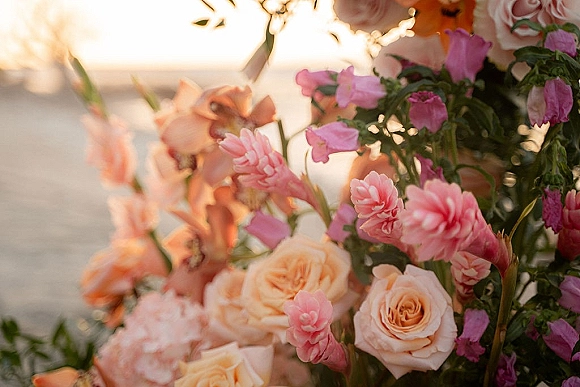 Wedding floral arrangement of peach and pink wedding flowers with roses and greenery, set against an ocean horizon under sunset sky