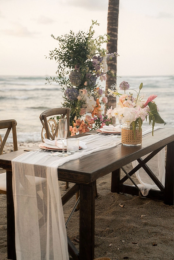 Reception tablescape with beach wedding tablescape details on a wooden table, pastel florals and votive candles by the ocean horizon﻿