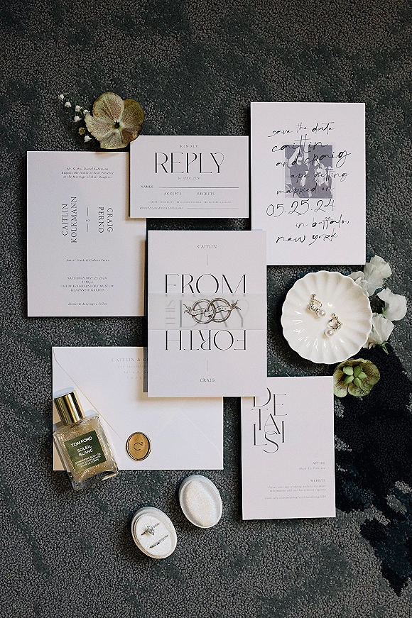 Invitation suite wedding invitation flat lay with envelope and wax seal, ring box, pearl earrings, perfume and flowers on a textured rug