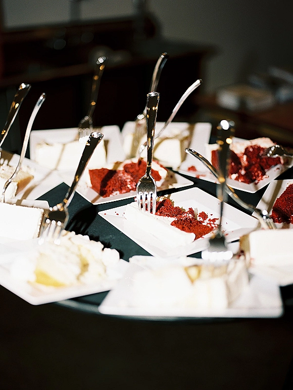 Wedding cake slices on plates with forks and cake server, buttercream frosting and crumbs on a dessert table against a dark backdrop