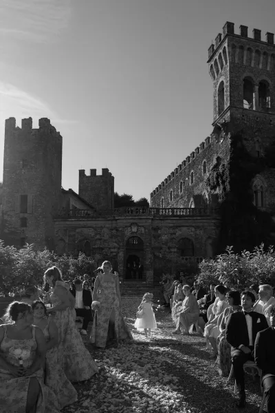Flower girl moment during the wedding processional as she tosses petals along a gravel aisle in a stone castle courtyard.