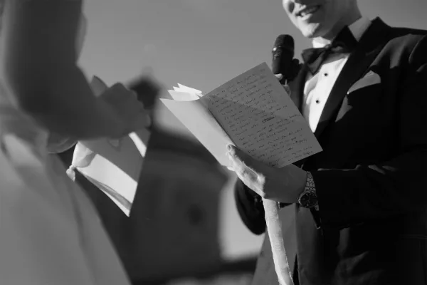 Wedding vows shared in an intimate ceremony moment as the groom reads from a small vow book, his voice steady while the bride listens.