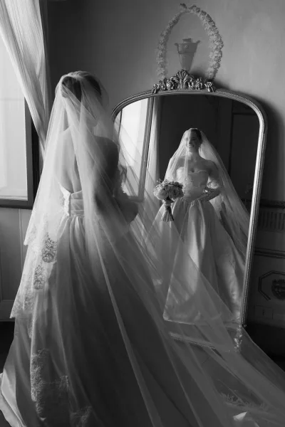Bridal portrait of a bride getting ready as she adjusts her veil, a timeless moment captured before the ceremony.