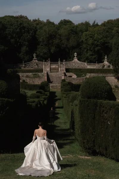 Bridal portrait in a formal garden, a garden bridal portrait of a bride with lace gloves by a stone staircase between trimmed hedges.