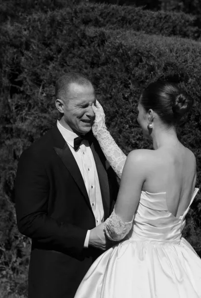 First look moment in an outdoor first look as the bride in lace gloves reaches for her groom amid garden hedges.