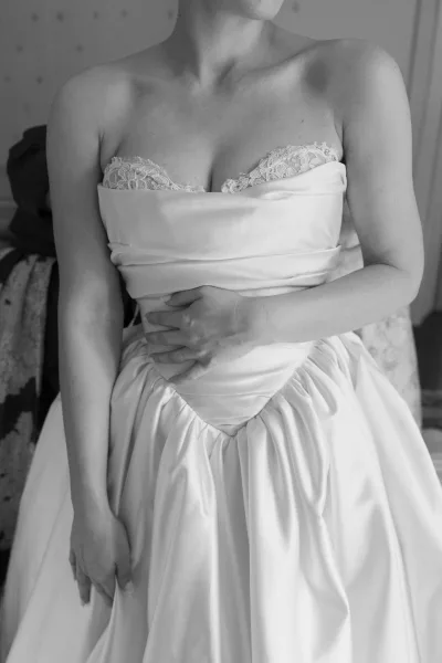 Wedding dress close-up of a strapless wedding dress with lace trim on the bodice, set against patterned wallpaper and an upholstered chair.