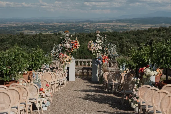 Ceremony setup for an outdoor garden ceremony featuring a floral arch on a terrace, framed by a mountain view and valley.