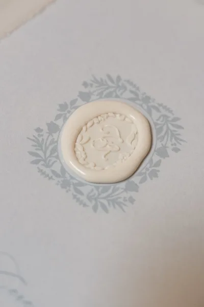 Wax seal showcasing a wedding invitation detail with a custom monogram crest, cleanly pressed on light blue paper.