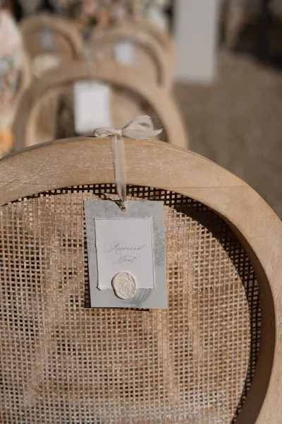 Reserved seat sign and wedding chair tag finished with a wax seal, hanging amid rows of chairs over gravel ground at the ceremony.